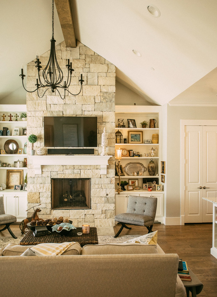 Offenes Klassisches Wohnzimmer mit beiger Wandfarbe, dunklem Holzboden, Kamin, Kaminumrandung aus Stein und TV-Wand in Dallas