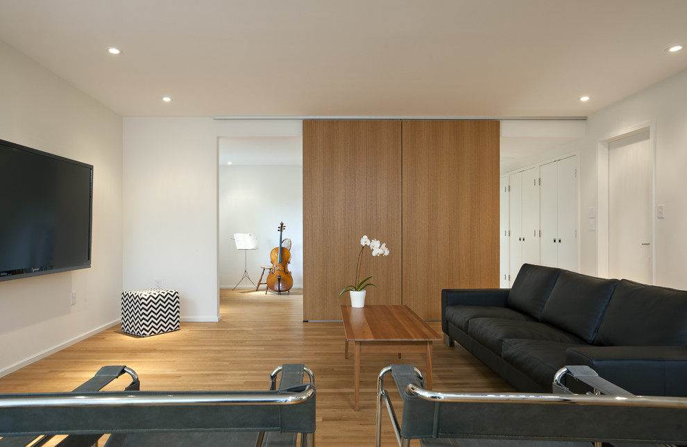 Foto de sala de estar minimalista con paredes blancas, suelo de madera en tonos medios y televisor colgado en la pared
