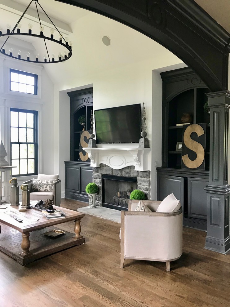This is an example of a medium sized bohemian open plan games room in Nashville with white walls, dark hardwood flooring, a standard fireplace, a stone fireplace surround, a wall mounted tv and brown floors.