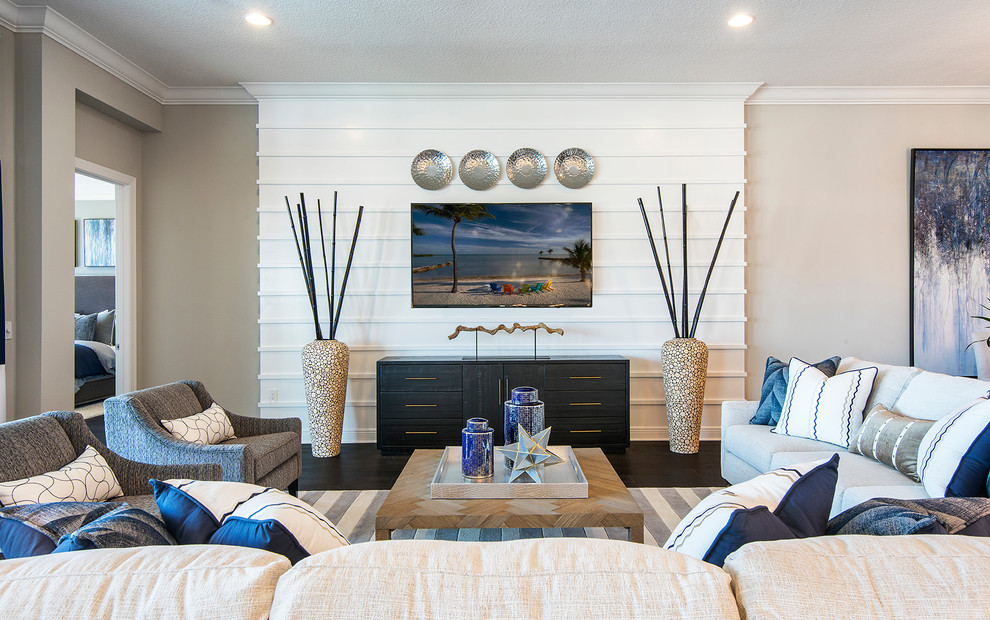Пример оригинального дизайна: открытая гостиная комната в морском стиле с серыми стенами, темным паркетным полом, коричневым полом, телевизором на стене и панелями на части стены