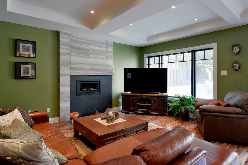 На фото: большая открытая гостиная комната в стиле кантри с зелеными стенами, паркетным полом среднего тона, стандартным камином, фасадом камина из плитки и телевизором в углу