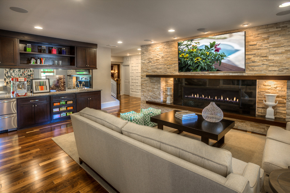 Imagen de sala de estar con barra de bar cerrada tradicional renovada grande con paredes beige, suelo de madera en tonos medios y televisor colgado en la pared