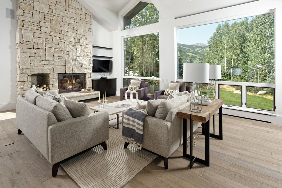 Cette photo montre une grande salle de séjour tendance ouverte avec un mur blanc, une cheminée standard, un manteau de cheminée en pierre, un téléviseur fixé au mur, un sol gris et un sol en bois brun.