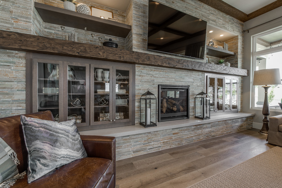 This is an example of a large traditional open plan games room in Salt Lake City with grey walls, light hardwood flooring, a standard fireplace, a stone fireplace surround, a wall mounted tv and brown floors.