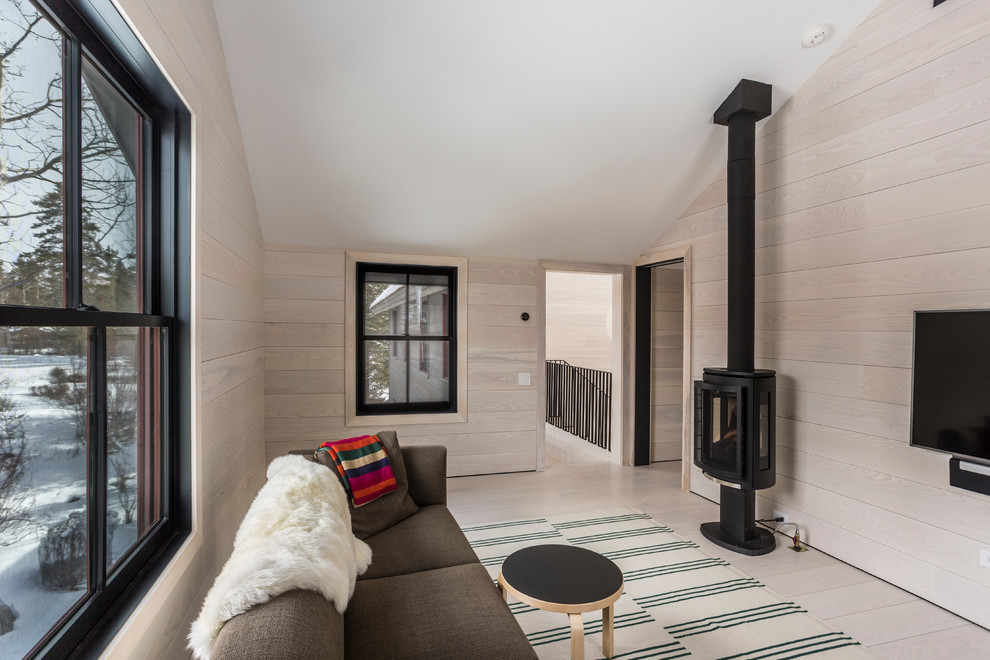 Imagen de sala de estar cerrada rústica con paredes beige, suelo de madera clara, estufa de leña, televisor colgado en la pared y suelo beige