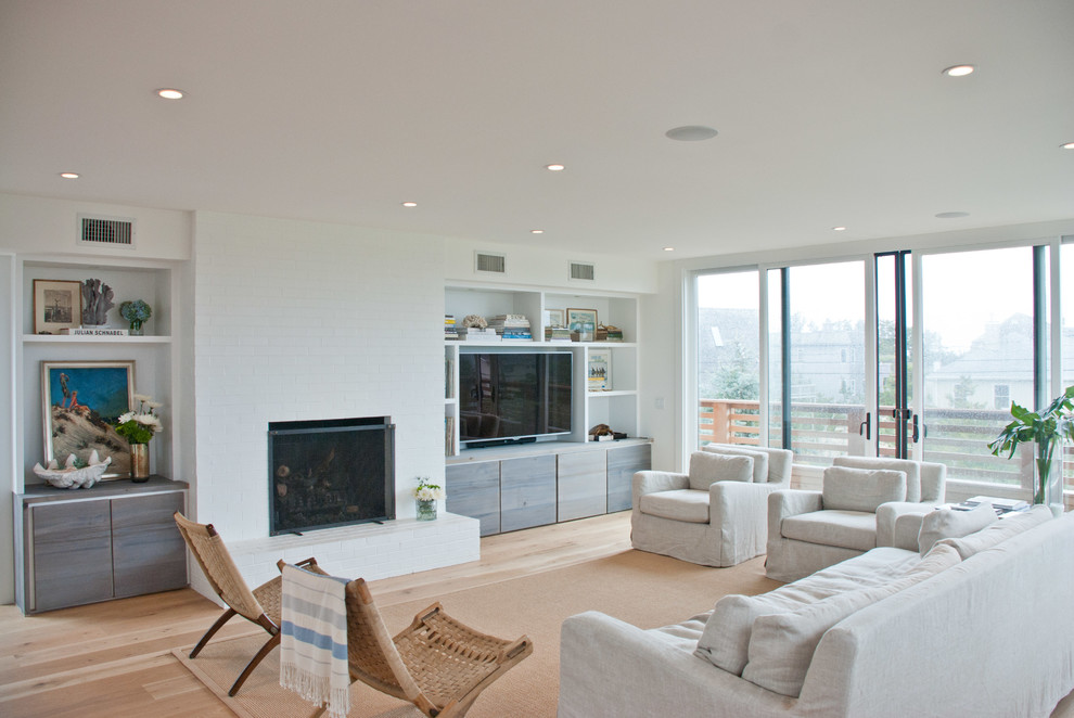 Стильный дизайн: открытая гостиная комната в современном стиле с белыми стенами, паркетным полом среднего тона, стандартным камином, фасадом камина из кирпича и телевизором на стене - последний тренд