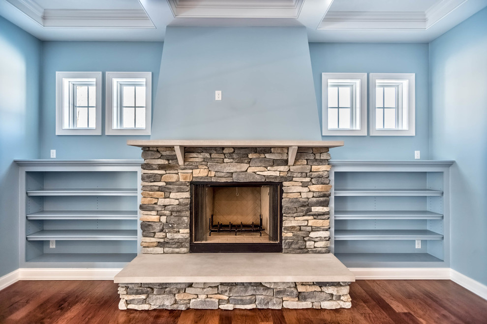 Modelo de sala de estar abierta tradicional grande con paredes azules, suelo de madera en tonos medios, todas las chimeneas, marco de chimenea de piedra, televisor colgado en la pared y suelo marrón