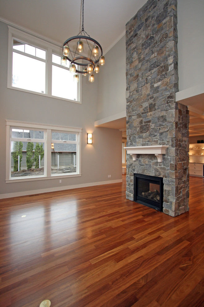 Photo of a large traditional open plan games room in Seattle with grey walls, medium hardwood flooring, a two-sided fireplace, a stone fireplace surround and a wall mounted tv.