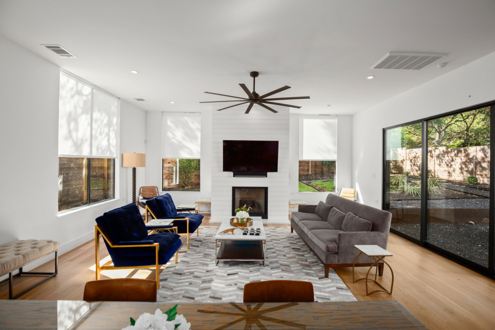 Mittelgroßes, Offenes Modernes Wohnzimmer mit weißer Wandfarbe, hellem Holzboden, Kamin, Kaminumrandung aus Holzdielen und TV-Wand in Austin