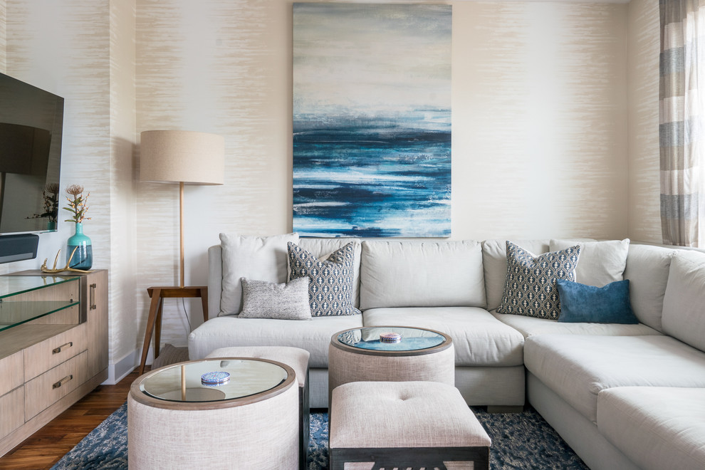 Modelo de sala de estar costera sin chimenea con paredes beige, suelo de madera oscura, televisor colgado en la pared y alfombra