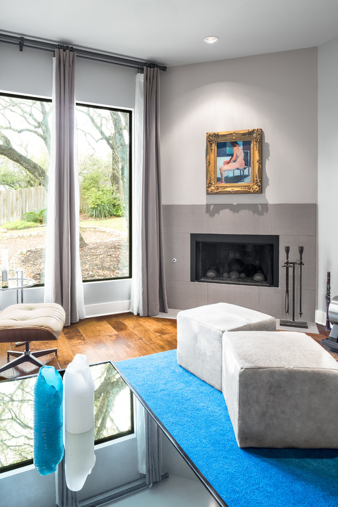 Cette photo montre une salle de séjour chic ouverte avec un mur gris, un sol en bois brun, une cheminée d'angle et un manteau de cheminée en carrelage.