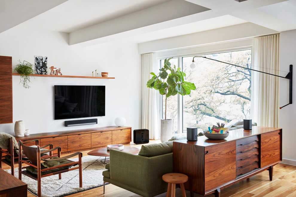 Пример оригинального дизайна: гостиная комната в современном стиле с белыми стенами, паркетным полом среднего тона, телевизором на стене и коричневым полом