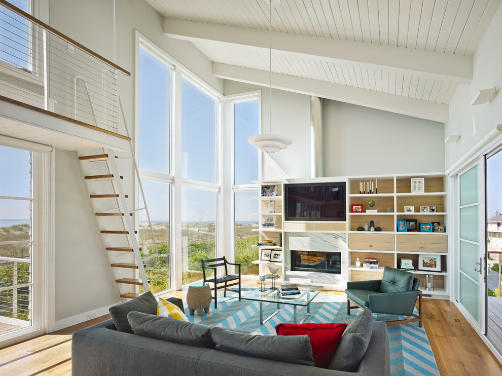 Ejemplo de sala de estar abierta marinera con paredes grises, suelo de madera en tonos medios, chimenea lineal, marco de chimenea de piedra y pared multimedia