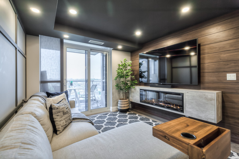 This is an example of a medium sized contemporary open plan games room in Toronto with grey walls, medium hardwood flooring, a hanging fireplace, a wooden fireplace surround, a wall mounted tv and grey floors.