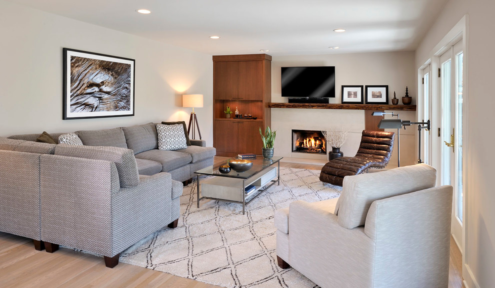 Imagen de sala de estar actual con paredes beige, suelo de madera clara, todas las chimeneas, televisor colgado en la pared y marco de chimenea de hormigón