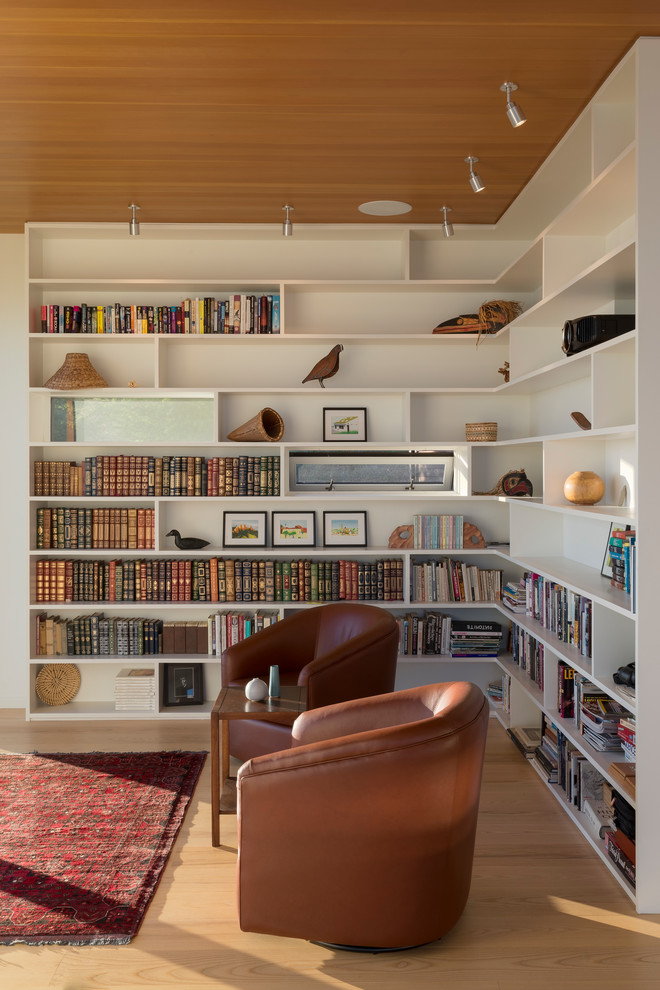 Foto på ett litet 60 tals allrum, med ett bibliotek, vita väggar, ljust trägolv och brunt golv