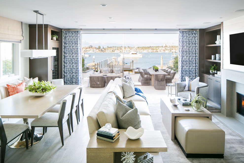 Inspiration for a nautical open plan games room in Orange County with white walls, light hardwood flooring, a standard fireplace, a concrete fireplace surround, a wall mounted tv and beige floors.