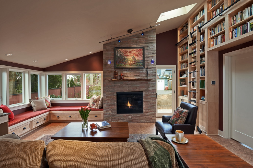 Imagen de sala de estar con biblioteca abierta de estilo americano de tamaño medio sin televisor con paredes rojas, suelo de corcho, marco de chimenea de piedra, todas las chimeneas y suelo marrón