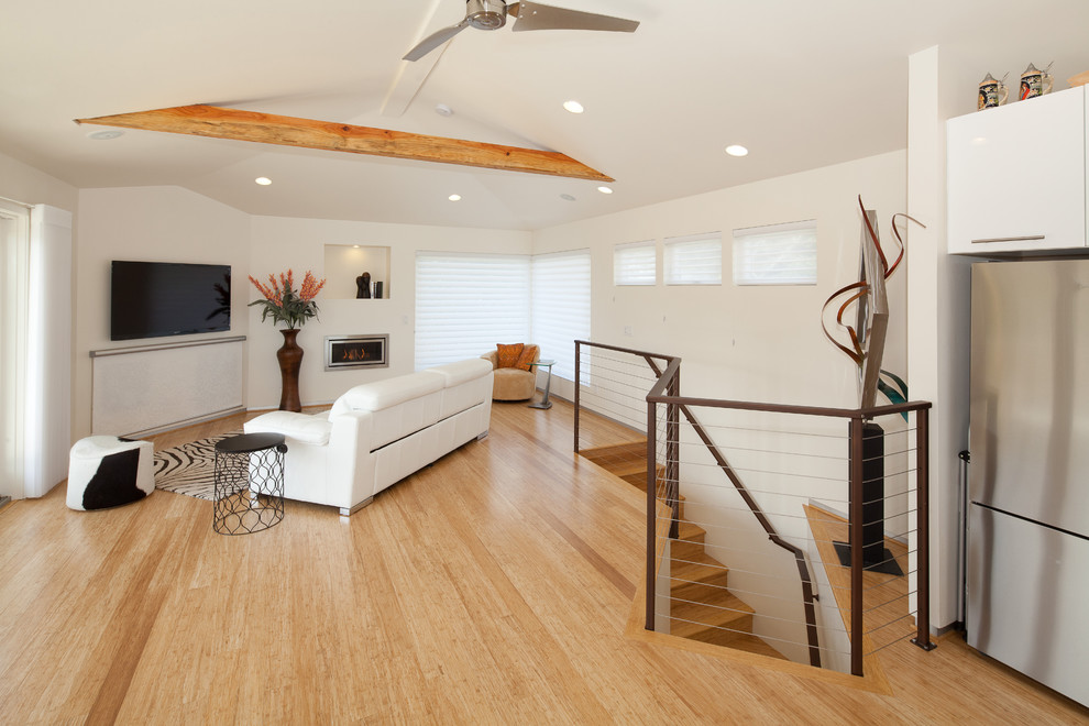 Example of a trendy loft-style light wood floor and beige floor family room design in San Luis Obispo with white walls, a wall-mounted tv and a standard fireplace