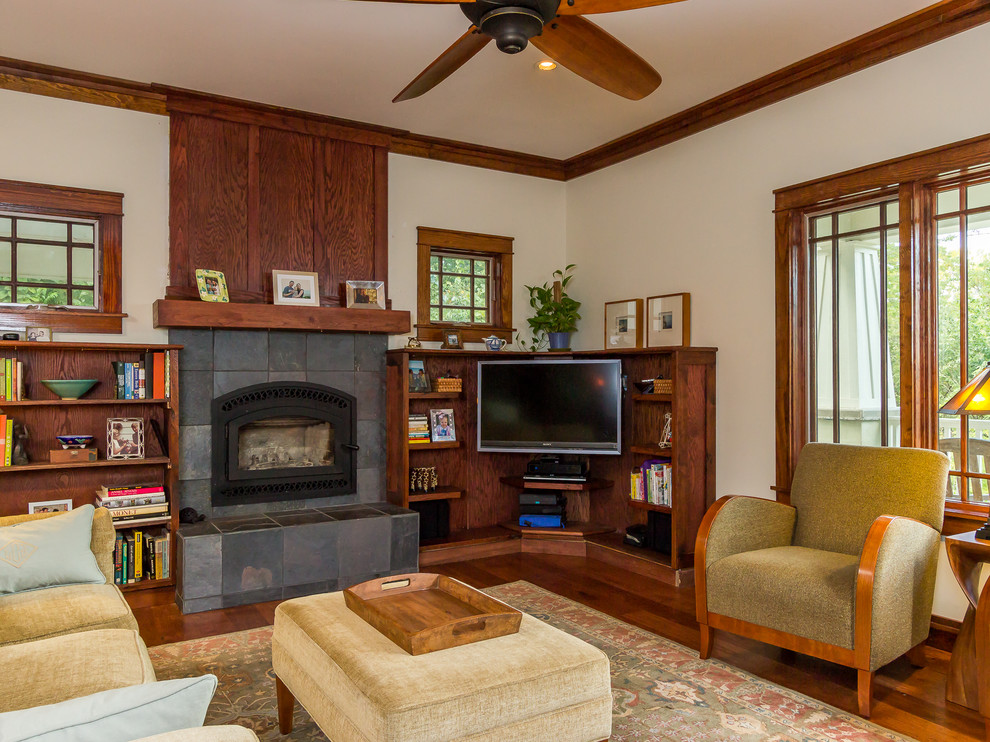 Idée de décoration pour une salle de séjour craftsman avec un mur beige, parquet foncé, une cheminée standard, un manteau de cheminée en pierre et un téléviseur d'angle.