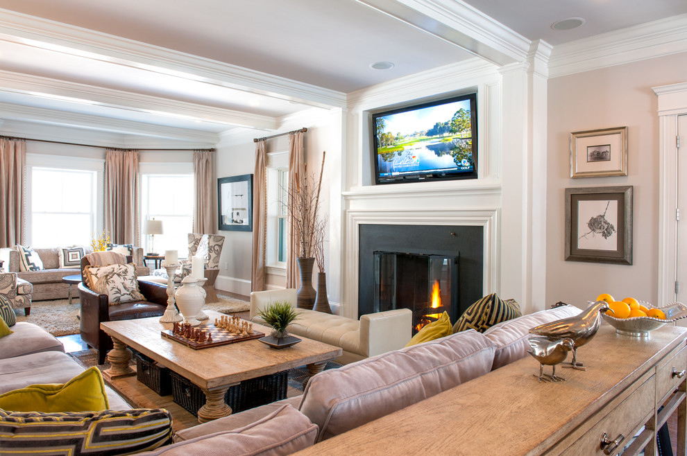 Cette image montre une grande salle de séjour traditionnelle ouverte avec un mur beige, un téléviseur fixé au mur, un sol en bois brun, une cheminée standard et un manteau de cheminée en métal.