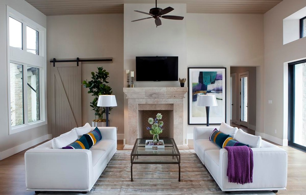 Offenes Modernes Wohnzimmer mit braunem Holzboden, Kamin, Kaminumrandung aus Stein, TV-Wand und beiger Wandfarbe in Austin