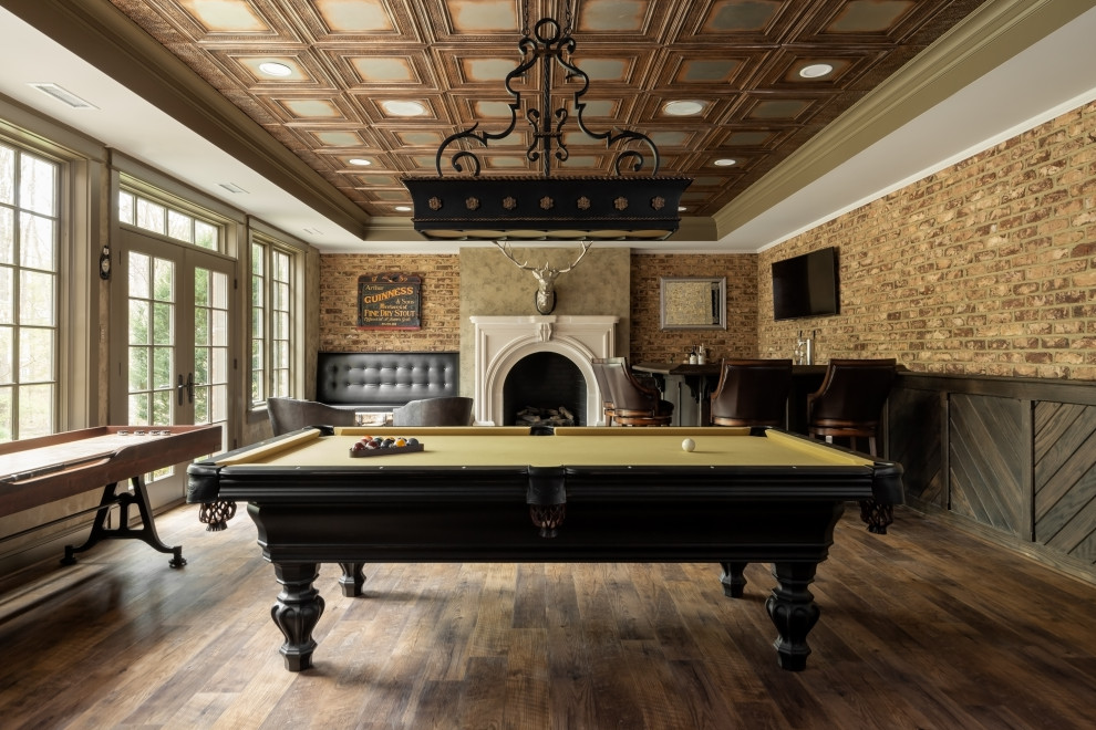 Large classic games room in Richmond with a game room, brown walls, medium hardwood flooring, a standard fireplace, a plastered fireplace surround, a wall mounted tv, brown floors and brick walls.