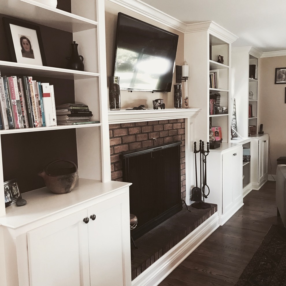 Cette photo montre une salle de séjour chic de taille moyenne et ouverte avec une bibliothèque ou un coin lecture, un mur beige, un sol en bois brun, une cheminée standard, un manteau de cheminée en brique, un téléviseur fixé au mur et un sol marron.