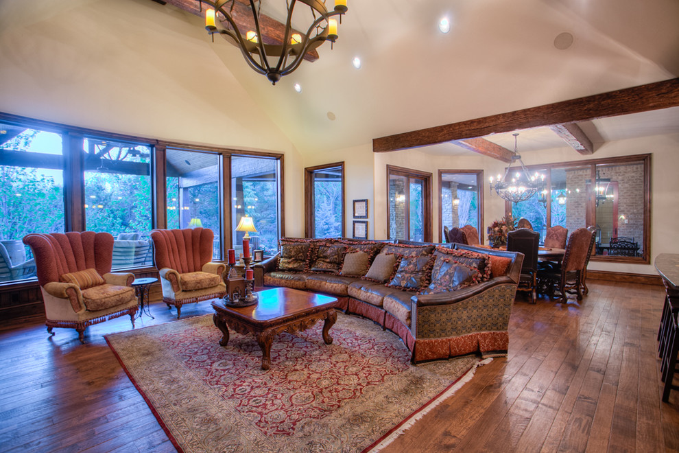 Example of a large mountain style open concept medium tone wood floor family room design in Oklahoma City with beige walls, a standard fireplace, a stone fireplace and a wall-mounted tv