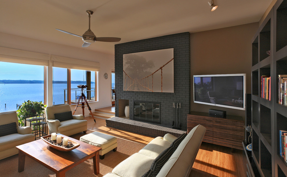 Cette image montre une salle de séjour design avec un mur beige, un sol en bois brun, une cheminée standard, un manteau de cheminée en brique et un téléviseur d'angle.