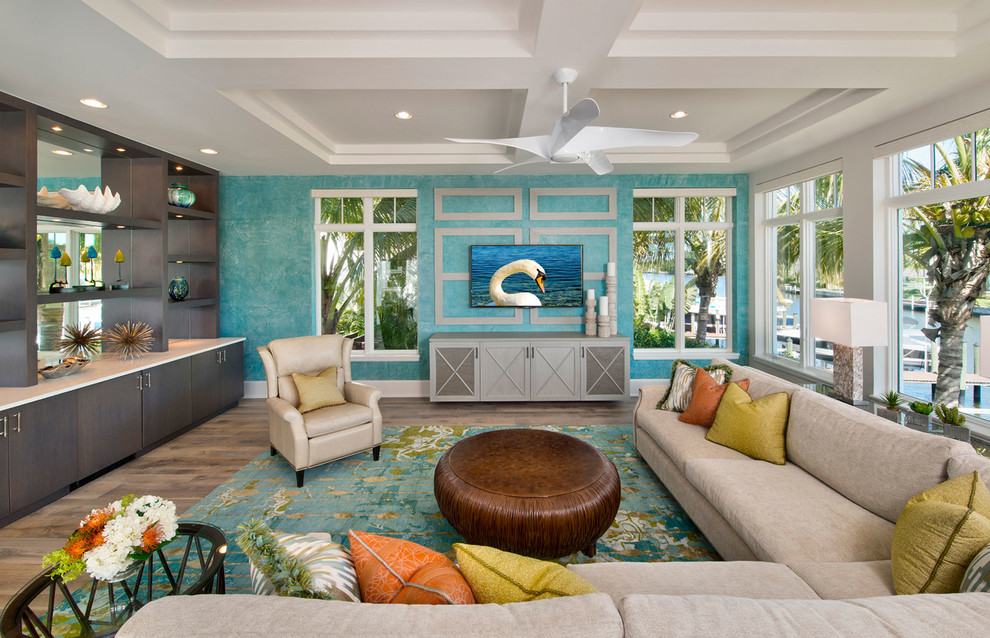 Пример оригинального дизайна: гостиная комната в морском стиле с синими стенами, паркетным полом среднего тона, телевизором на стене, коричневым полом и акцентной стеной без камина
