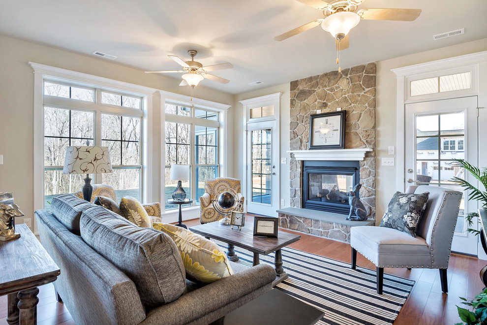 Diseño de sala de estar abierta de estilo americano de tamaño medio con paredes beige, suelo de madera en tonos medios, todas las chimeneas y marco de chimenea de piedra