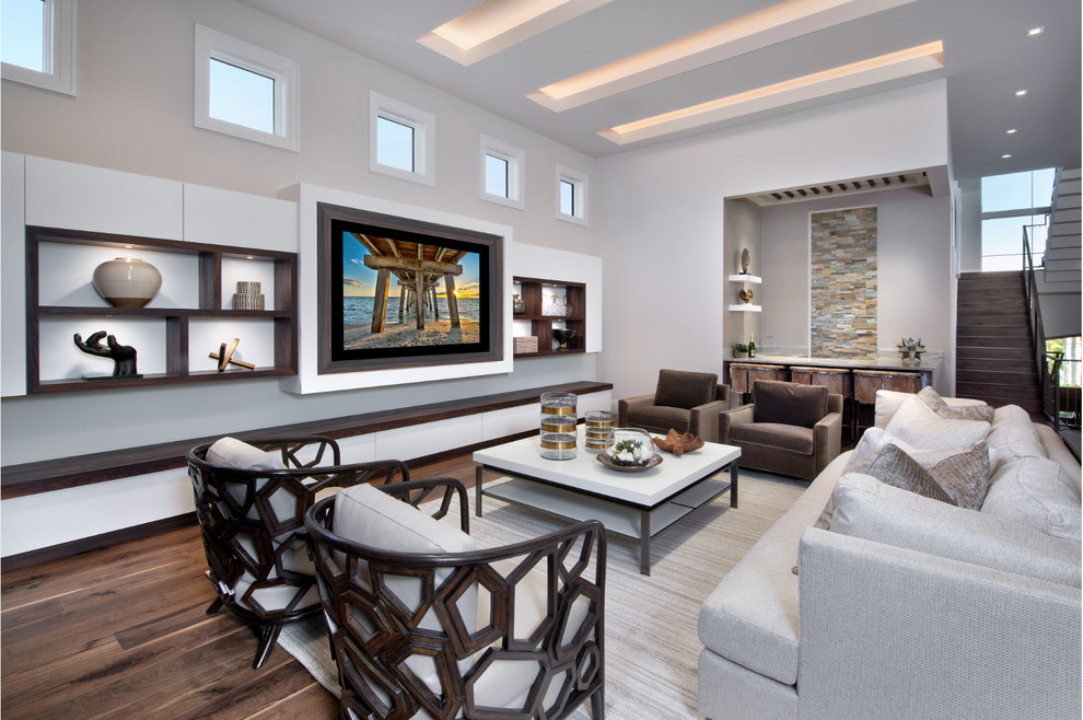 Photo of a large contemporary open plan games room in Miami with a home bar, grey walls, medium hardwood flooring, no fireplace, a wall mounted tv and brown floors.