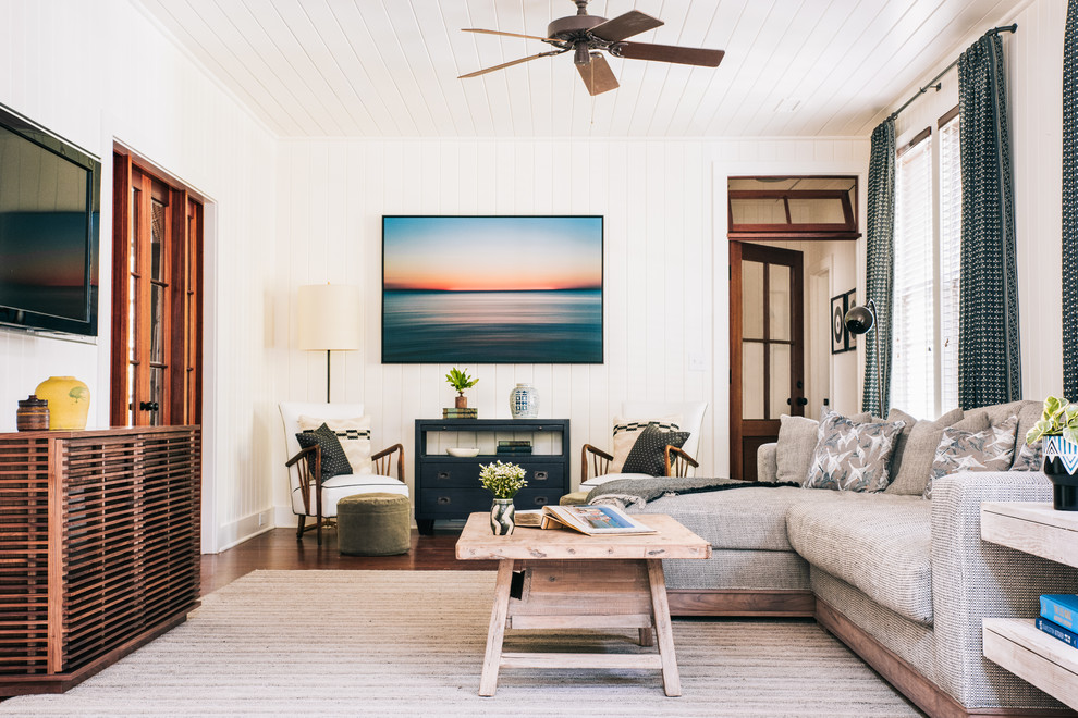 Modelo de sala de estar marinera con paredes blancas, suelo de madera oscura, televisor colgado en la pared y suelo marrón