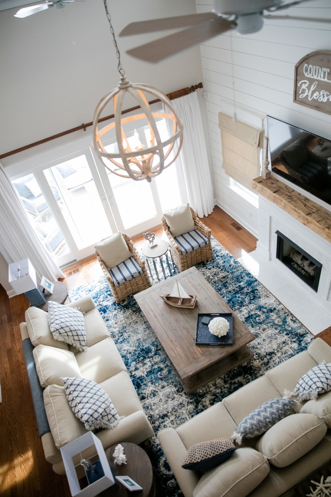 На фото: гостиная комната в морском стиле с серыми стенами, паркетным полом среднего тона, стандартным камином, фасадом камина из плитки, телевизором на стене и коричневым полом