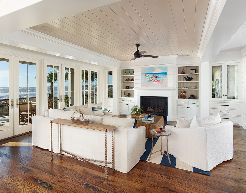 Ejemplo de sala de estar abierta costera con suelo de madera en tonos medios y marco de chimenea de piedra