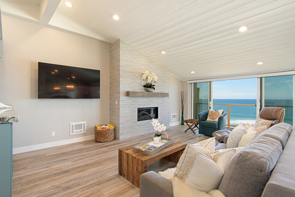 Cette image montre une salle de séjour marine de taille moyenne et ouverte avec un mur gris, un sol en vinyl, une cheminée standard, un manteau de cheminée en carrelage, un téléviseur fixé au mur et un sol gris.
