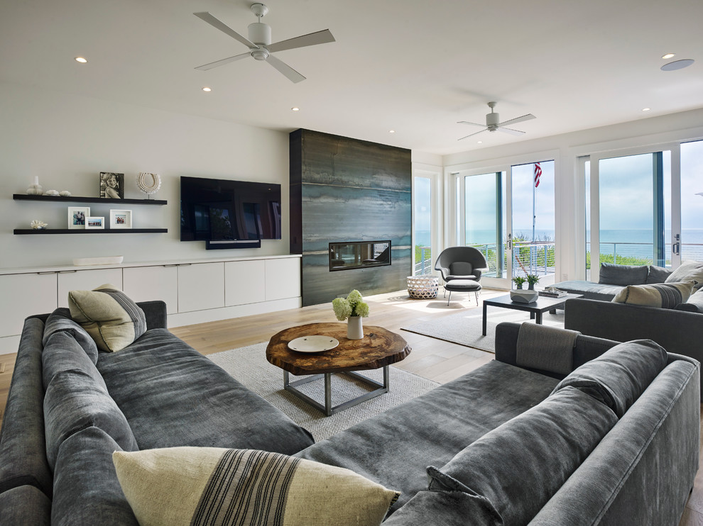 Diseño de sala de estar abierta contemporánea grande con paredes blancas, suelo de madera clara, chimenea lineal, marco de chimenea de metal, suelo amarillo y televisor colgado en la pared