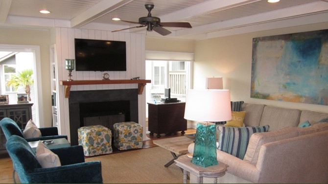 Imagen de sala de estar abierta marinera grande con paredes beige, suelo de madera en tonos medios, todas las chimeneas y televisor colgado en la pared