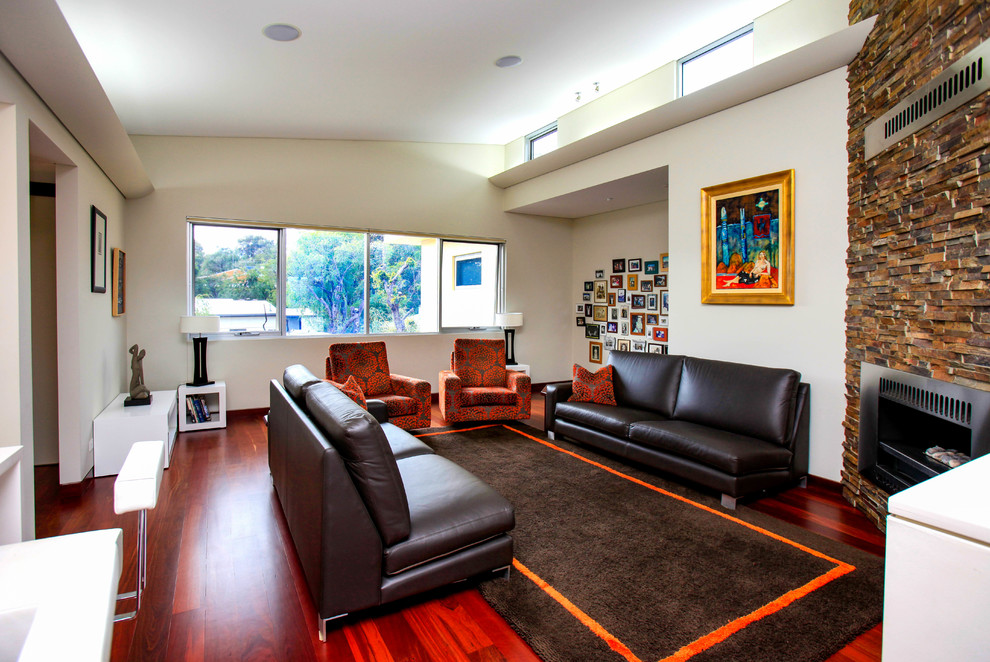 Cette photo montre une grande salle de séjour ouverte avec un mur multicolore, un sol en bois brun, cheminée suspendue, un manteau de cheminée en pierre, un téléviseur dissimulé et un sol rouge.