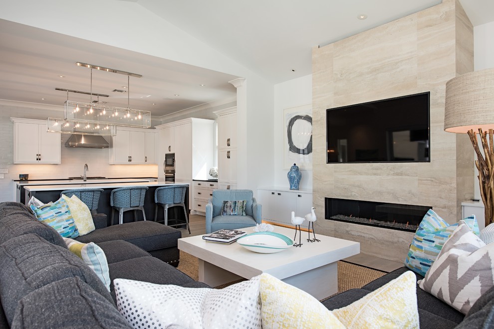 Diseño de sala de estar abierta costera con paredes blancas, chimenea lineal, marco de chimenea de piedra y televisor colgado en la pared