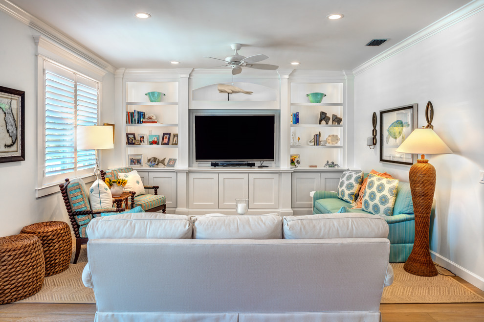 Diseño de sala de estar cerrada costera con paredes blancas, suelo de madera en tonos medios, televisor colgado en la pared y suelo marrón