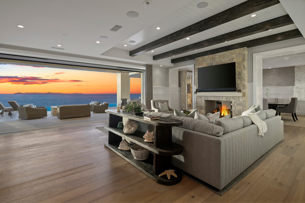 На фото: гостиная комната в морском стиле с паркетным полом среднего тона, двусторонним камином, телевизором на стене и коричневым полом с