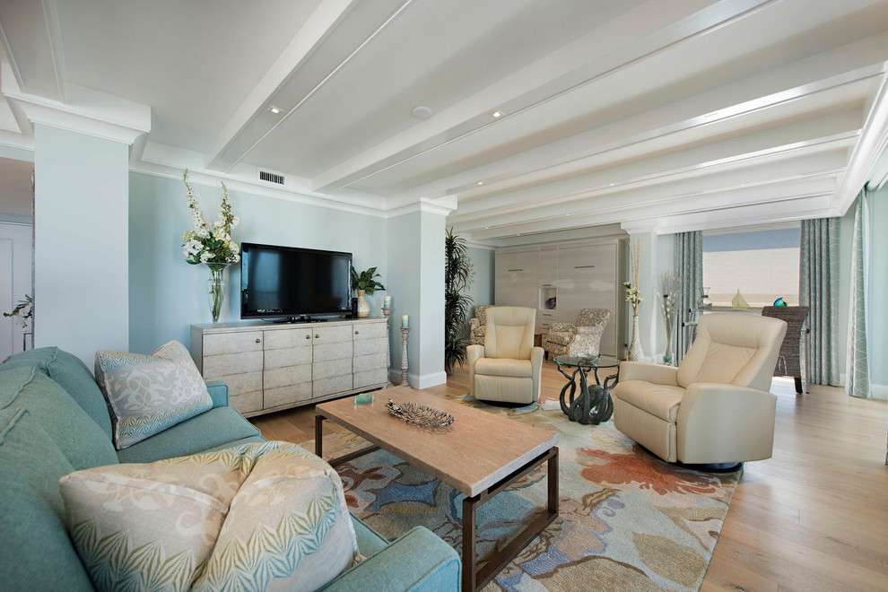 На фото: большая двухуровневая гостиная комната в морском стиле с с книжными шкафами и полками, синими стенами, светлым паркетным полом, телевизором на стене, бежевым полом и ковром на полу без камина с