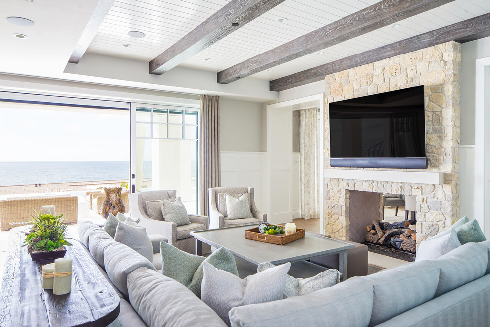 Beach style open concept medium tone wood floor and brown floor family room photo in Orange County with gray walls, a two-sided fireplace, a stone fireplace and a wall-mounted tv