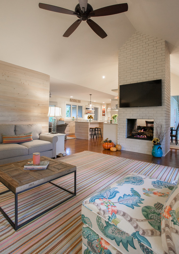 Offenes Maritimes Wohnzimmer mit braunem Holzboden, Tunnelkamin, Kaminumrandung aus Backstein und TV-Wand in Charleston