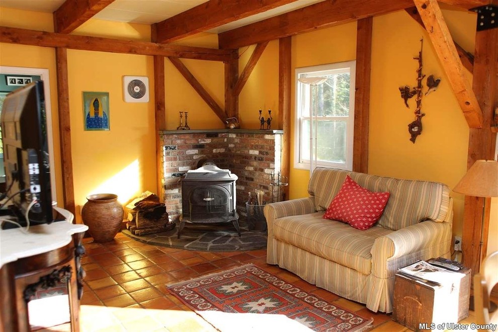 Imagen de sala de estar abierta bohemia de tamaño medio con paredes amarillas, suelo de baldosas de terracota, chimenea de esquina, marco de chimenea de piedra y televisor independiente