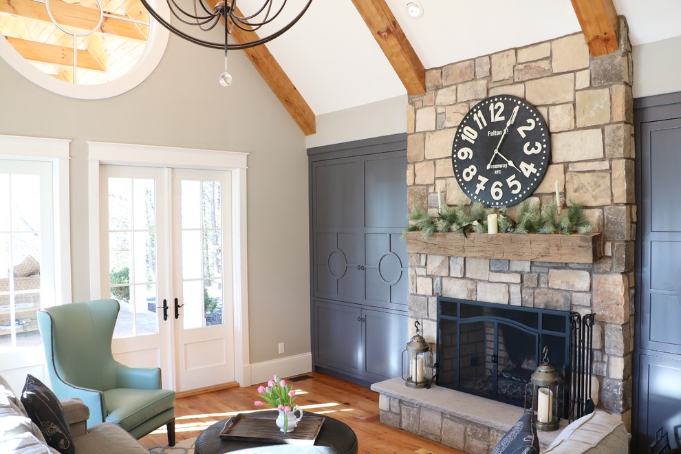 Idée de décoration pour une grande salle de séjour champêtre fermée avec un mur gris, un sol en bois brun, une cheminée standard, un manteau de cheminée en pierre et un téléviseur encastré.