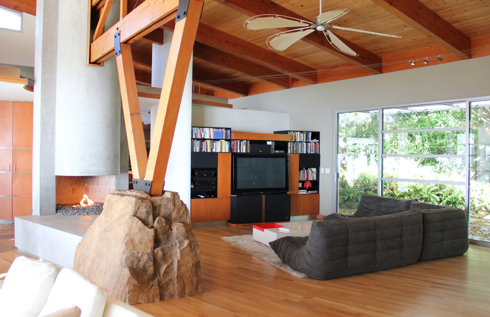 This is an example of a large modern open plan games room in Los Angeles with a game room, light hardwood flooring, a hanging fireplace, a concrete fireplace surround and a built-in media unit.