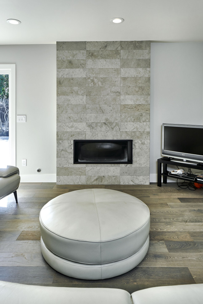 Пример оригинального дизайна: открытая гостиная комната среднего размера в стиле модернизм с серыми стенами, паркетным полом среднего тона, стандартным камином, фасадом камина из камня, телевизором в углу и серым полом
